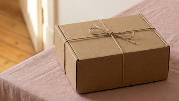 Plain discreet brown parcel tied with twine on a dusty-rose linen surface — 1sttoy discreet shipping in New Zealand