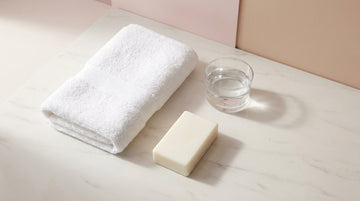 Folded white towel, a bar of soap and a glass of water on a marble surface — clean, body-safe sex toy care