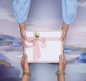 Two hands sharing a small wrapped gift on a warm-toned background — couples intimacy and considered choice.