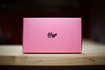 A pastel pink wrapped gift box on a warm wooden table — festive, understated, no fuss.